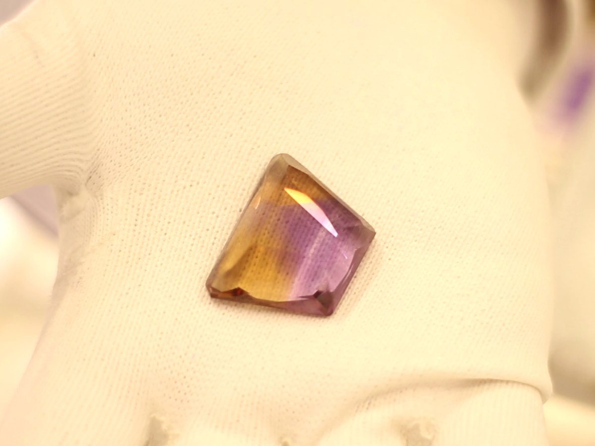 Amétrine taillée, violette et jaune, posée dans une main gantée